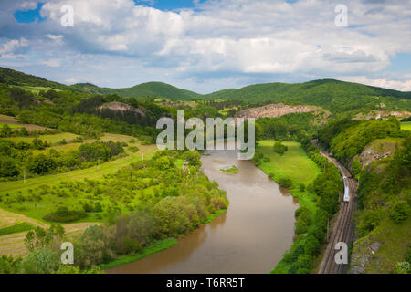 Blick vom Hügel in das Tal mit dem Fluss Berounka. Fluss Berounka, Kalksteinfelsen, Wiesen, Felder und Eisenbahn. Stockfoto