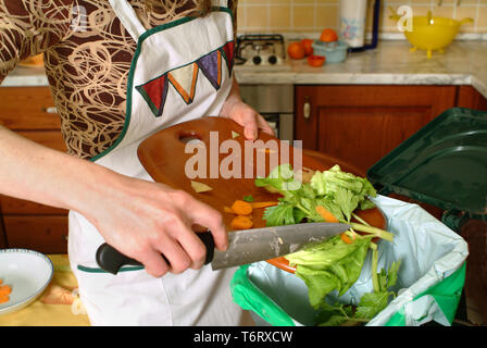 Detail einer weiblichen Hand Entsorgung der organischen Abfälle in einem geeigneten Behälter mit Küche im Hintergrund Stockfoto