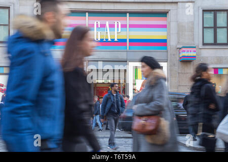 Käufer in der Oxford Street im West End von London vorbei an einem Zweig von Gap Kleidung Store im Winter Stockfoto