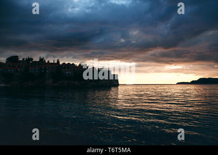 Blick auf das Meer und die Insel Sveti Stefan auf dem Hintergrund der Sonnenuntergang in Montenegro. Dies ist eine der wichtigsten Sehenswürdigkeiten von Montenegro. Stockfoto