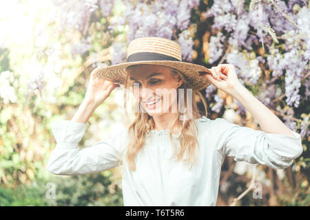 Lachend Kaukasischen blonde Mädchen close-up im hellen Sonnenlicht vor dem Hintergrund einer Wisteria blühen. Leniy Konzept, Tourismus und Urlaub. Stockfoto