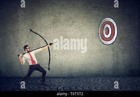 Bestimmt business Mann, der versucht, ein Ziel sein Ziel mit Pfeil und Bogen zu schlagen Stockfoto