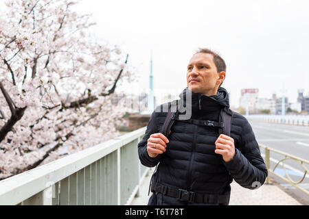 Tokio, Japan Sumida Asakusa district Stadtbild Skyline auf Brücke mit jungen Touristen Mann suchen am Kirschblüte in Downtown an bewölkten Stockfoto