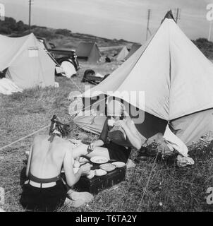 Camping in den 1940er Jahren. Ein Campingplatz, wo die Menschen Teile ihrer Sommerurlaub verbringen. Das Gelände ist voll von Zelten. Zwei junge Frauen sitzen vor ihrem Zelt essen und trinken Kaffee. Schweden 1940 Stockfoto