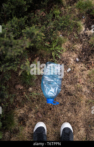 Mann gefunden ständigen Füße - Blau großen Kunststoff Flasche auf dem Boden liegend in Baum in einem Park Wald geworfen, die nicht recycelt - Abfall und Verschmutzung der Stockfoto