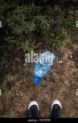 Mann gefunden ständigen Füße - Blau großen Kunststoff Flasche auf dem Boden liegend in Baum in einem Park Wald geworfen, die nicht recycelt - Abfall und Verschmutzung der Stockfoto