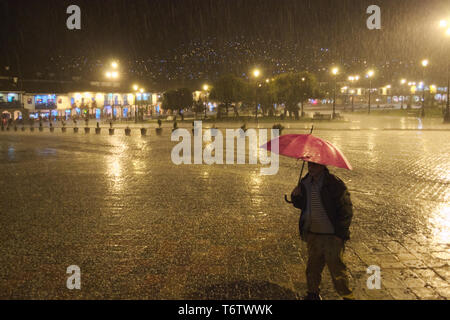 Ein Mann in der Nacht mit einem Regenschirm in der Nähe des Hauptplatzes in Cusco, Peru, während eines Sturms. Stockfoto