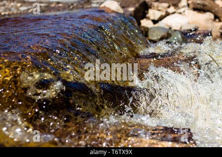 Sauberer Fluss fließt das Wasser über die Steine und umhüllt Sie. Die hellen Sonnenstrahlen sind in das fließende Wasser und verraten seine Brillanz wider. Stockfoto