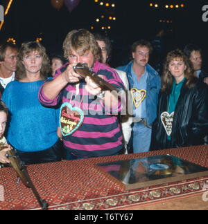 Der deutsche Fernsehmoderator, Entertainer, Wis, Hörbuchsprecher, Musiker und Komiker Jürgen von der Lippe eine Einems Schießstand auf einer Kirmes, Deutschland 1980er. Der Deutsche Fernsehmoderator, Entertainer, Schauspieler, Sprecher, Musiker und Komiker Jürgen von der Lippe zu einem Shooting Gallery an Karneval, Deutschland der 80er Jahre. Stockfoto