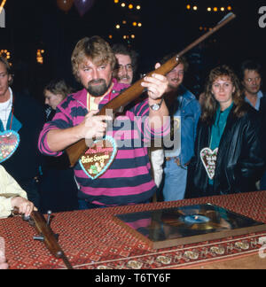 Der deutsche Fernsehmoderator, Entertainer, Wis, Hörbuchsprecher, Musiker und Komiker Jürgen von der Lippe eine Einems Schießstand auf einer Kirmes, Deutschland 1980er. Der Deutsche Fernsehmoderator, Entertainer, Schauspieler, Sprecher, Musiker und Komiker Jürgen von der Lippe zu einem Shooting Gallery an Karneval, Deutschland der 80er Jahre. Stockfoto