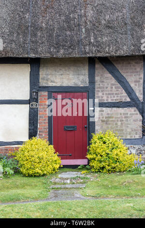 Traditionelle englische Reetdachhaus Eingang mit der roten Tür Stockfoto