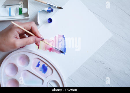 Satz von Aquarellfarben, Pinsel und Palette auf einem weißen Blatt, die Hand der Frau zeichnet wunderschöne Aquarell Anschläge, Hintergrund oder Konzept Stockfoto