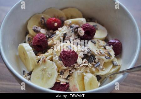 Frische Früchte in eine Schüssel Müsli, lecker Frühstück mit Haferflocken, Milch, Himbeeren und Bananen Stockfoto