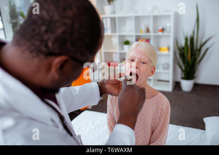 Dunkelhäutige Arzt untersuchen Kehle von Schulmädchen schlechte Gefühl Stockfoto