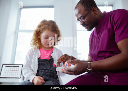 Süße kleine lockige Mädchen Pillen nehmen vom angenehmen Kinderarzt Stockfoto