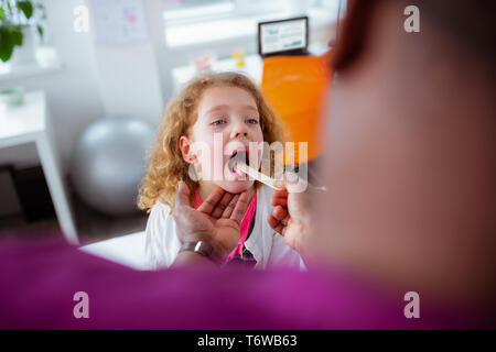 Curly ansprechende kleine Mädchen öffnen den Mund für Kinderarzt Stockfoto