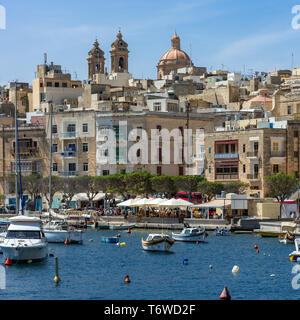 Die baumgesäumte Uferpromenade von Senglea in Malta mit ihren historischen Kalksteingebäuden, die zu den zwei Glockentürmen und der Kuppel der Senglea-Basilika führen Stockfoto