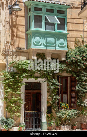 Ein malerisches Haus in Il-Birgu mit seinem traditionellen, von Gallarija umgebenen Holzbalkon und grünem Laub um die Eingangstür Stockfoto