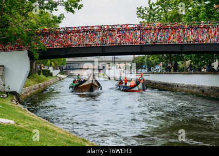 Aveiro, Portugal - 29. April 2019: traditionelles Boot, Moliceiro, Transport von Touristen vorbei unter Brücke in Konfetti bedeckt auf Kanal bei Aveiro. Stockfoto