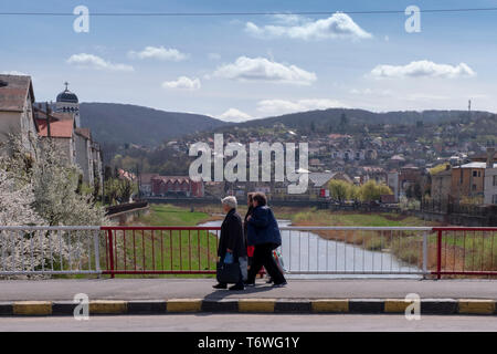 Alba Iulia, Rumänien - 9. April 2019: Drei alten Damen gehen auf der Brücke über den Fluss Tarnava in Sighisoara. Blick auf die Türme der alten Gebäude Stockfoto