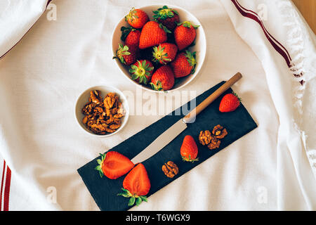 Blick von oben auf eine saftige frische Erdbeeren und Muttern mit einem Messer, der mit einem weißen Hintergrund. Gesundes Frühstück oder Dessert. Stockfoto