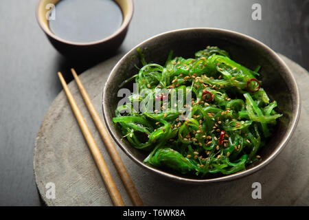 Wakame Algen Salat mit Sesam und Chili Pfeffer in einer Schüssel auf einem hölzernen Slice Stockfoto