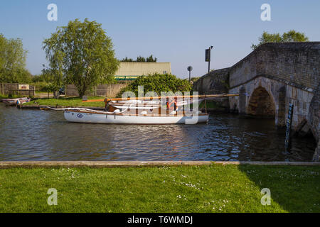 Ein Boot mit eingezogenem Mast auf dem Fluss Thurne durch einen niedrigen Stein mittelalterliche Brücke in Potter Heigham, Norfolk, Großbritannien navigiert Stockfoto