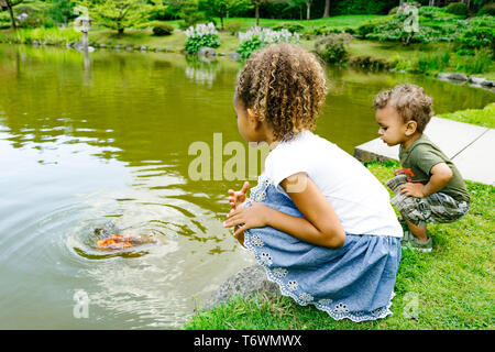 Ein junges Mädchen und Jungen sitzen durch einen Teich an einem öffentlichen Park Stockfoto