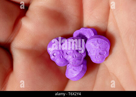 Topview des Palm der kaukasischen Hand mit einem kleinen Haufen von lila Armee Schädel, Ecstasy, MDMA, Amphetaminen oder Medikamente wie ein Schädel geformt Stockfoto