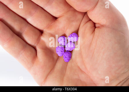 Topview des Palm der kaukasischen Hand mit einem kleinen Haufen von lila Armee Schädel, Ecstasy, MDMA, Amphetaminen oder Medikamente wie ein Schädel geformt Stockfoto