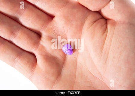 Topview des Palm von einer weißen männlichen Hand mit etwas lila XTC, MDMA, Amphetamin oder Medikamente Pille wie ein Schädel geprägt. Stockfoto