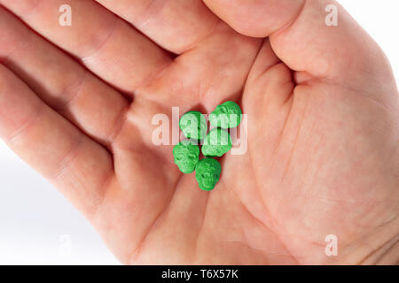 Topview palm kaukasischen männliche Hand mit einem kleinen Haufen grün Schädel, Ecstasy, MDMA, Amphetaminen oder Medikamente wie ein Schädel geprägt. Stockfoto