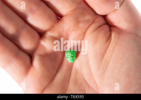 Topview des Palm von einer weißen männlichen Hand mit einem kleinen grünen XTC, MDMA, Amphetamin oder Medikamente Pille wie ein Schädel geprägt. Stockfoto