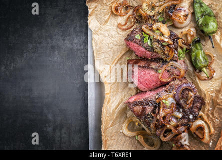 Traditionelle deutsche Grill geschnitten Zwiebelrostbraten mit gebratenen Zwiebeln und grünen Paprika als Draufsicht auf Trägerpapier in Einem Stockfoto