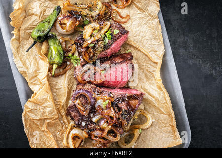 Traditionelle deutsche Grill geschnitten Zwiebelrostbraten mit gebratenen Zwiebeln und grünen Paprika als Draufsicht auf Trägerpapier in Einem Stockfoto