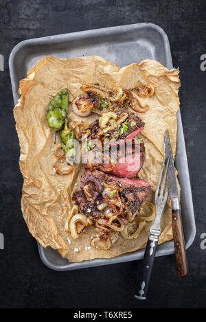 Traditionelle deutsche Grill geschnitten Zwiebelrostbraten mit gebratenen Zwiebeln und grünen Paprika als Draufsicht auf Trägerpapier in Einem Stockfoto