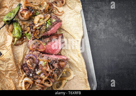 Traditionelle deutsche Grill geschnitten Zwiebelrostbraten mit gebratenen Zwiebeln und grünen Paprika als Draufsicht auf Trägerpapier in Einem Stockfoto