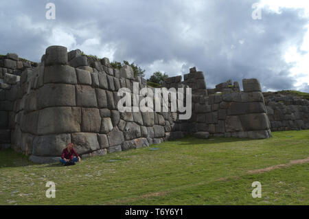 Blick auf das riesige Mauern der Ruinen von Sacsayhuaman in Cusco, Peru. Ein Mädchen sitzt an der Wand der massenhaften Bauweise zu zeigen. Stockfoto