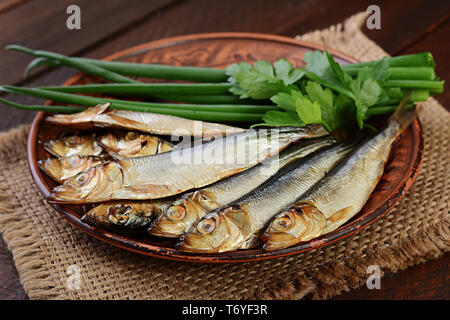 Geräucherte Sprotten und grüne Zwiebel auf einem Schneidebrett auf einer hölzernen Hintergrund. Geräucherten Fisch. Stockfoto