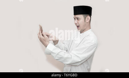 Portrait von Stattlichen asiatischen muslimischen Mann mit Kopf und mit Smartphone und lassen Sie sich überraschen - Bild Stockfoto