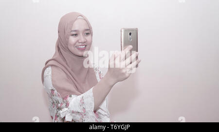 Portrait von asiatischen muslimische Frau mit Kopftuch oder hijab Sie Ihr Smartphone unter selfie, Anruf- und Videokonferenz - Bild Stockfoto