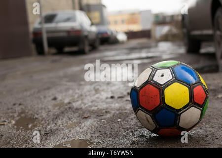 Fußball für Kinder ball spiel ist auf eine schmutzige kaputte Straße Straße unter Pfützen und wohnyards von Häusern, in der Nähe von geparkten Autos Stockfoto