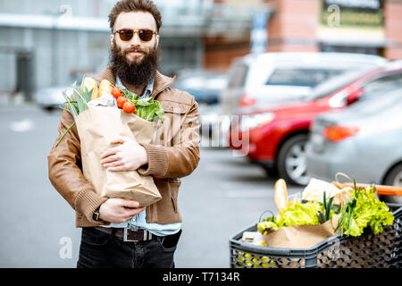 Gerne stilvolle Mann mit Tüten voller Frische und gesunde Lebensmittel im Freien in der Nähe der Supermarkt Stockfoto