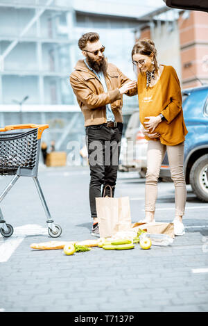 Mann Hilfe für junge schwangere Frau schlechte Gefühl auf dem Parkplatz in der Nähe der Supermarkt Stockfoto