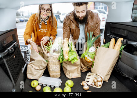 Junges Paar packen Tüten mit frischen Lebensmitteln in den Kofferraum, Ansicht vom Fahrzeuginnenraum Stockfoto