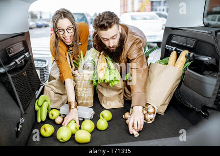 Junges Paar packen Tüten mit frischen Lebensmitteln in den Kofferraum, Ansicht vom Fahrzeuginnenraum Stockfoto