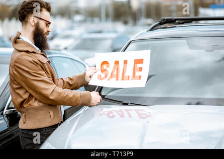 Stilvolle bärtige Verkäufer mit einem Umsatz Platte in der Nähe der Autos, die auf dem Boden einer Händlerniederlassung öffnen Stockfoto