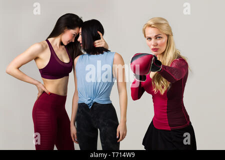 Junge passende Frau in Boxhandschuhen auf dem Hintergrund von zwei sportliche Mädchen posieren. Gegner. Wunsch zu gewinnen Stockfoto