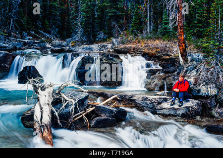 Frau sitzt neben einem Wasserfall. Stockfoto