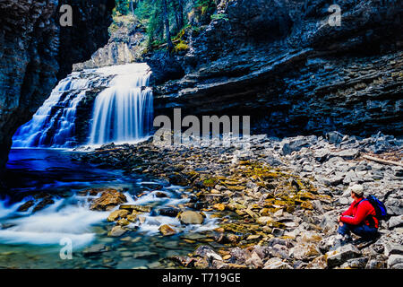 Frau sitzt neben einem Wasserfall. Stockfoto